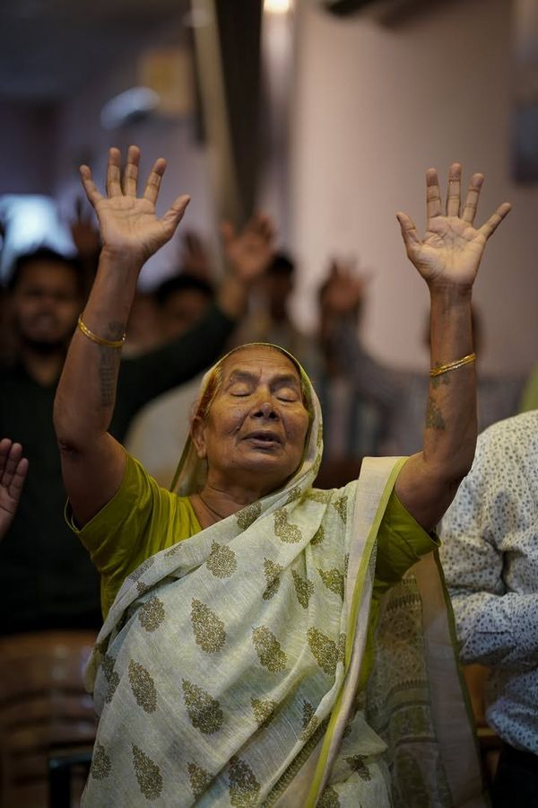An older woman praying with both hands lifted