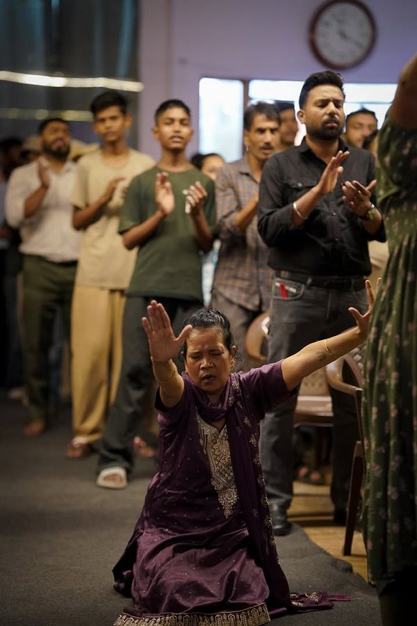 A woman kneeling to pray while the row behind her stands